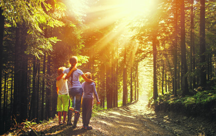 ©istock ©istock / Une femme et deux enfants en forêt regardent le soleil qui perce à travers les arbres